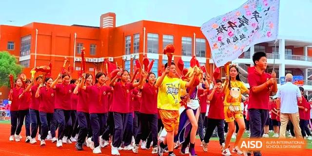 A student in a yellow jersey carries a ceremonial torch while leading a cheering crowd of classmates at Xiwai International School.