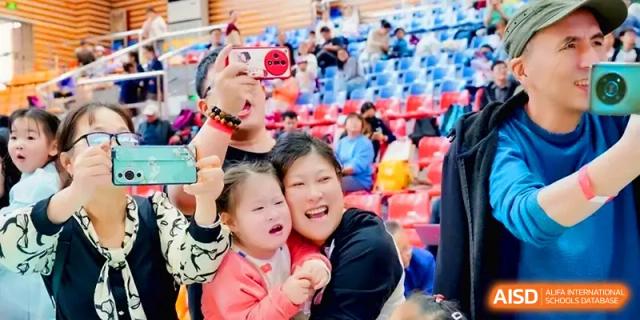 An adult and a young child watch an exciting school performance from the bleachers at Xiwai International School.