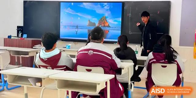 Students in maroon uniforms sit at their desks facing a large digital screen displaying a landscape at Xuzhou No.1 Middle School.