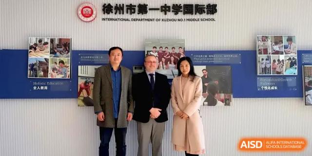 Three professionals pose together for a photo in front of an international department banner at Xuzhou No.1 Middle School.
