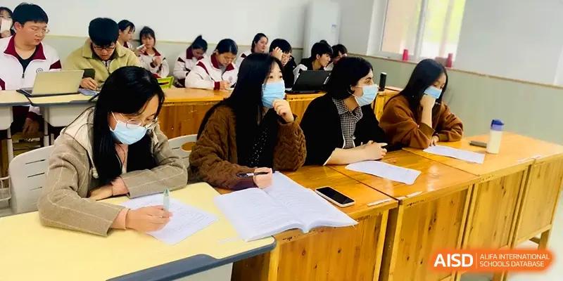 Students wearing face masks sit at wooden desks while focusing on their textbooks during a lesson at Xuzhou No.1 Middle School.