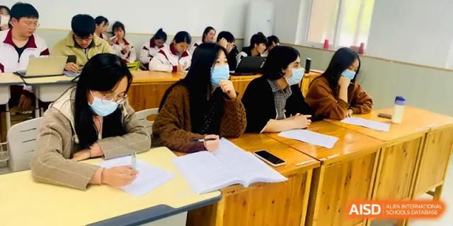 Students wearing face masks sit at wooden desks while focusing on their textbooks during a lesson at Xuzhou No.1 Middle School.