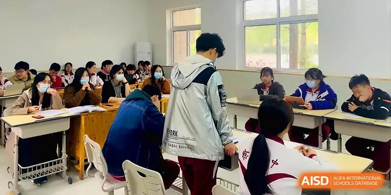 Students gather in a bright classroom, some standing and others sitting, during a collaborative break at Xuzhou No.1 Middle School.