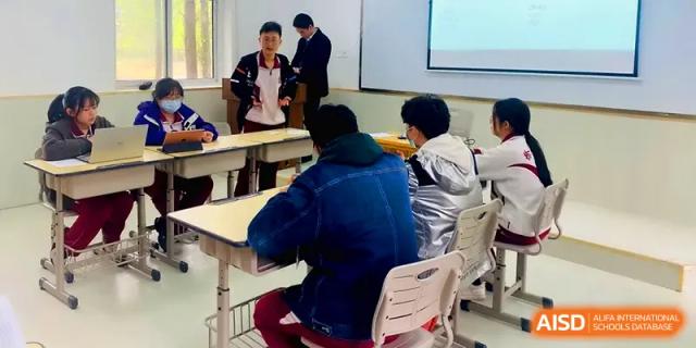 A student stands at the front of the class to give a presentation to their peers in a modern classroom at Xuzhou No.1 Middle School.