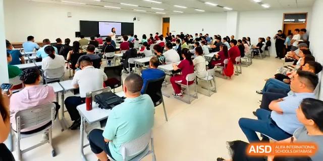 Rows of students are seen from behind as they listen to a presentation in a large, well-lit academic hall at Xuzhou No.1 Middle School.