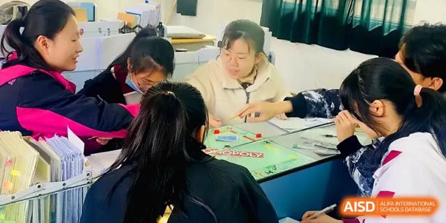 Three students huddle together over a board game, smiling and engaging in a strategic activity at Xuzhou No.1 Middle School.