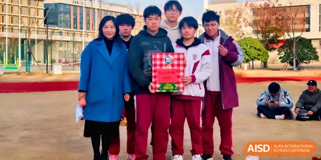 A group of students in red uniforms proudly displays a framed certificate with their teacher at Xuzhou No.1 Middle School.