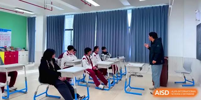 Students in maroon uniforms sit at white desks in a classroom with blue curtains, following a lesson at Xuzhou No.1 Middle School.