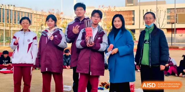 Students pose with a teacher while holding a trophy after a successful competition at Xuzhou No.1 Middle School.