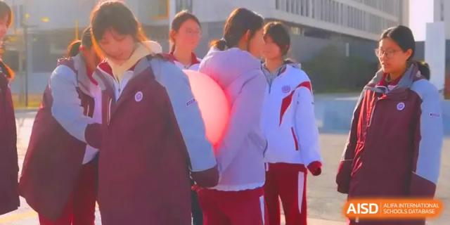 Two students coordinate their movements to hold a large glowing ball between them outdoors at Xuzhou No.1 Middle School.