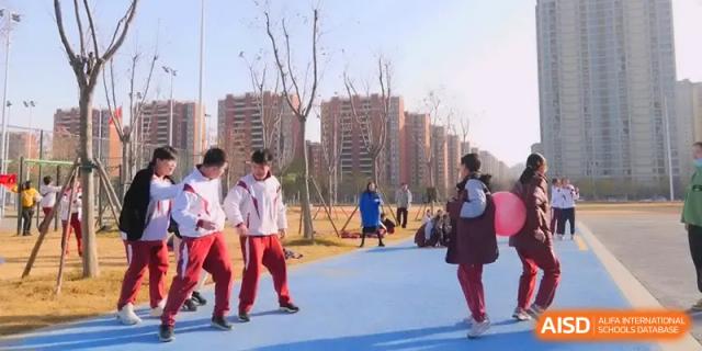 Students in maroon and white tracksuits participate in outdoor coordination games on a blue court at Xuzhou No.1 Middle School.