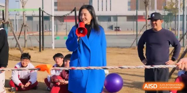 A teacher in a blue coat uses a megaphone to coordinate an outdoor sports festival for students at Xuzhou No.1 Middle School.