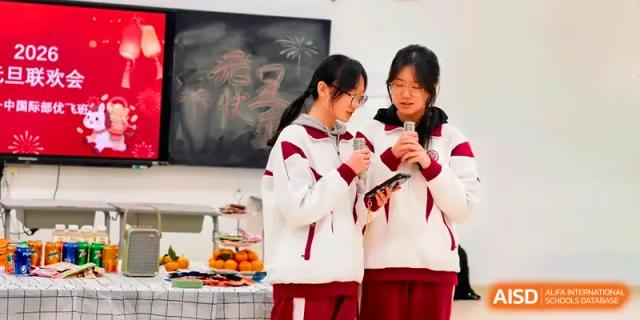 Two students in tracksuits hold microphones and read from a phone during a classroom celebration at Xuzhou No.1 Middle School.