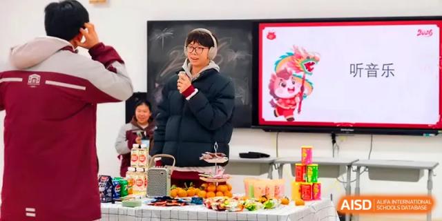 A student in a puffer jacket speaks into a microphone behind a table filled with holiday treats at Xuzhou No.1 Middle School.