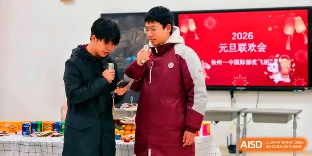 Two students stand at the front of the room, one singing into a microphone during a celebration at Xuzhou No.1 Middle School.