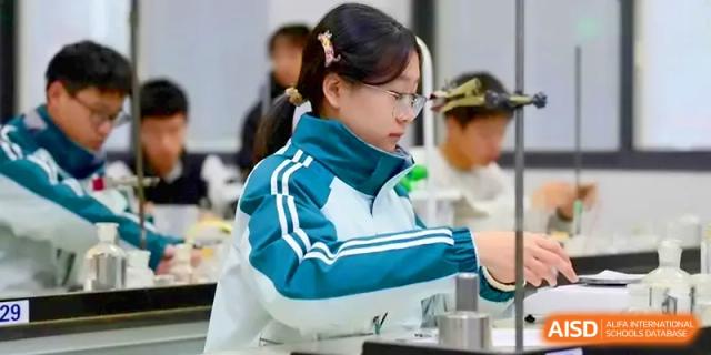A student in a teal tracksuit carefully performs a science experiment in a well-equipped lab at Yangzhou High School of Jiangsu Province.