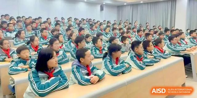A large class of students in matching teal tracksuits sits in tiered seating, listening to a lecture at Yangzhou High School of Jiangsu Province.