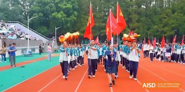 A student procession marches across a sports field carrying red flags and a ceremonial torch at Yangzhou High School of Jiangsu Province.