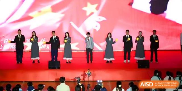 Four student vocalists perform together on a red stage in front of a large festive backdrop at Yangzhou High School of Jiangsu Province.