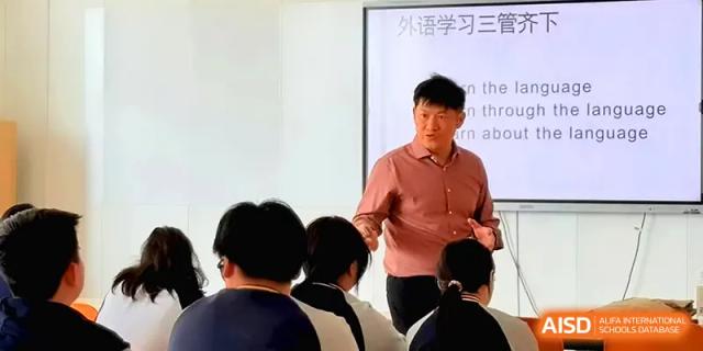 A male instructor in a red shirt leads a classroom discussion, engaging with students during a dynamic lecture session at Beijing Xinxuedao Linchuan School.