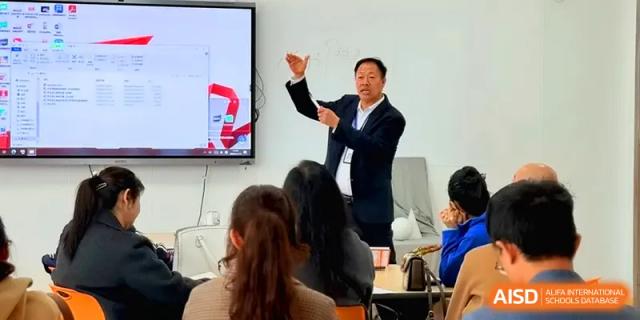 A male teacher in a suit gestures during an engaging classroom lecture while students listen attentively at Beijing Xinxuedao Linchuan School.