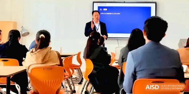 A professional presenter stands by a digital monitor, delivering an informative seminar to an audience of seated students at Beijing Xinxuedao Linchuan School.