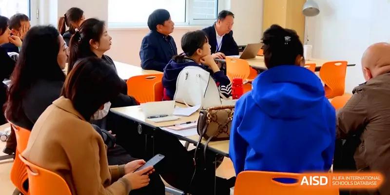 A group of students and faculty engage in an attentive meeting, discussing academic progress in a comfortable classroom at Beijing Xinxuedao Linchuan School.