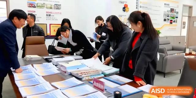 Staff members and teachers gather around a table to review and organize student workbooks and records at Beijing Xinxuedao Linchuan School.
