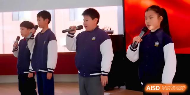 A young male student sings or speaks into a microphone during a talent show or school assembly at Beijing Xinxuedao Linchuan School.