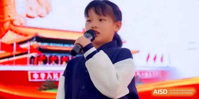 A young female student speaks confidently into a microphone while wearing her school uniform during a presentation at Beijing Xinxuedao Linchuan School.