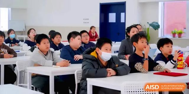 Students sit at their desks in a modern classroom, focusing on their teacher during a daily lesson at Beijing Xinxuedao Linchuan School.