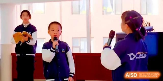 A young student holds a microphone and participates in a public speaking exercise during a class at Beijing Xinxuedao Linchuan School.