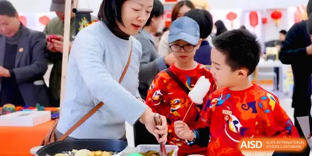 A teacher and students interact at a food stall during an outdoor festival featuring traditional snacks at Beijing Xinxuedao Linchuan School.