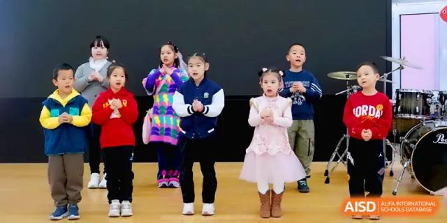 Young children perform a dance routine on stage in colorful costumes for their peers and parents at Beijing Xinxuedao Linchuan School.