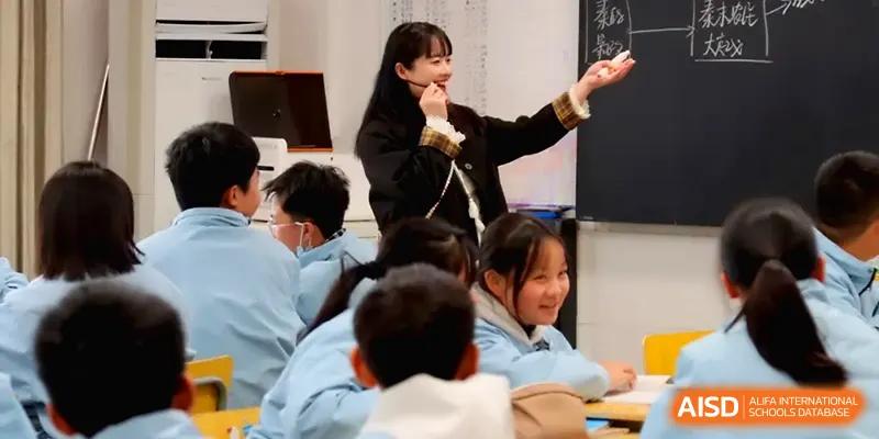 A cheerful teacher gestures while leading a lively classroom discussion with students in their blue uniforms at Changsha Mingda Middle School.