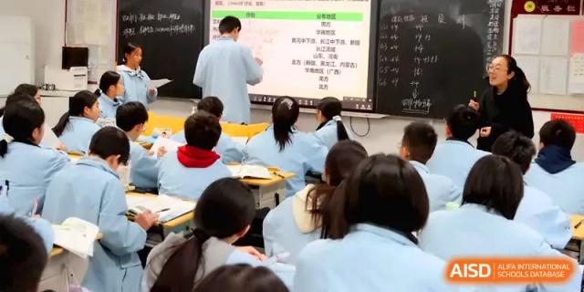 Students focus on a digital presentation while an instructor points to key information on the screen during class at Changsha Mingda Middle School.