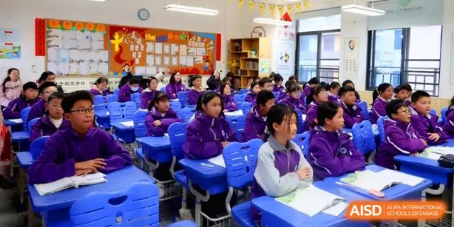 Rows of students in purple jackets sit at bright blue desks, listening intently to a lecture in a well-equipped room at Changsha Mingda Middle School.