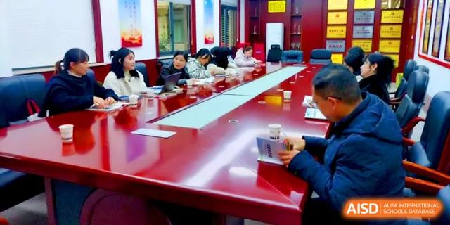 Staff members sit around a long red conference table for a formal administrative meeting in a professional office setting at Changsha Mingda Middle School.