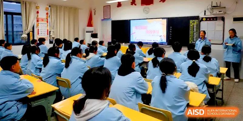A large group of students in light blue uniforms watches an educational video on a large screen at the front of the hall at Changsha Mingda Middle School.