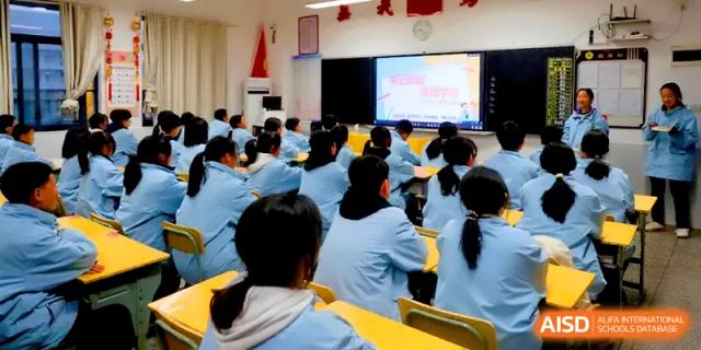 A large group of students in light blue uniforms watches an educational video on a large screen at the front of the hall at Changsha Mingda Middle School.