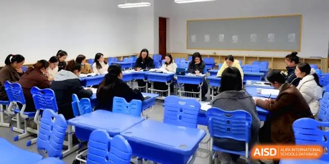 Teachers and staff sit in a circle of blue desks to conduct a collaborative faculty meeting and planning session at Changsha Mingda Middle School.