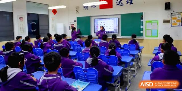 Students in purple uniforms sit at blue desks facing a digital whiteboard during an interactive multimedia lesson at Changsha Mingda Middle School.