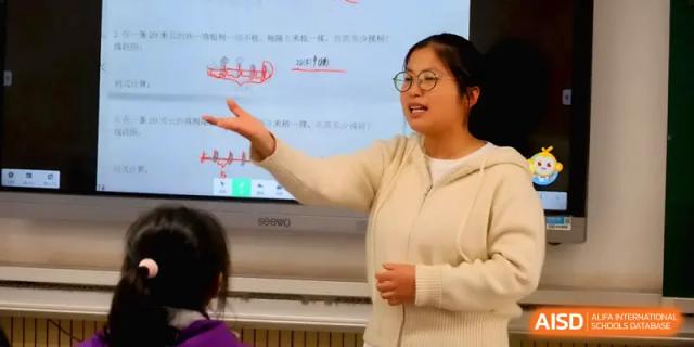 A teacher gestures toward a digital screen while explaining a lesson to her class in a bright, modern classroom at Changsha Mingda Middle School.