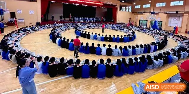 A massive group of students sits in concentric circles on the gymnasium floor for a large-scale event at Changsha Mingda Middle School.