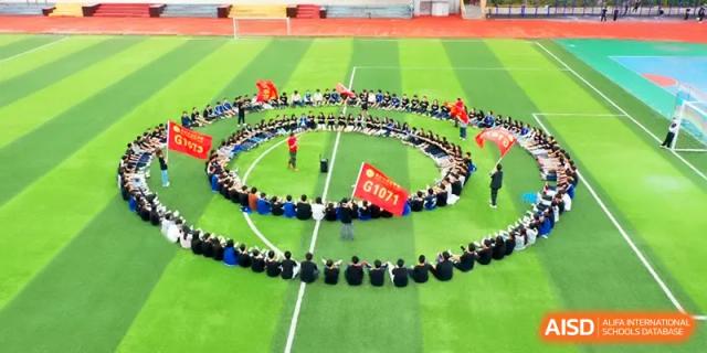 Students sit in a large circular formation on the green turf field during a supervised outdoor activity at Changsha Mingda Middle School.