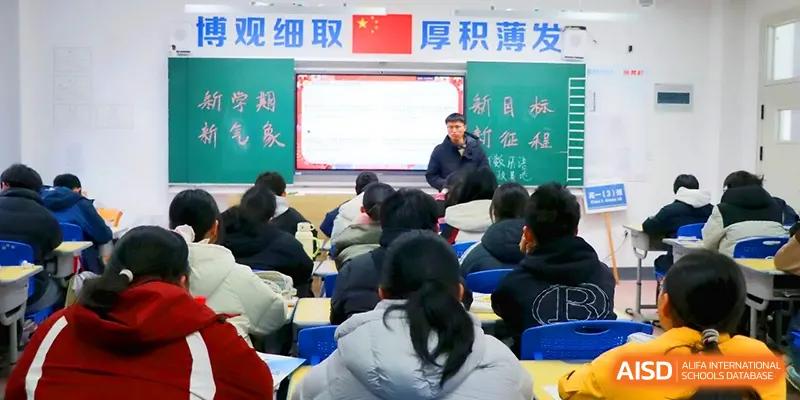 Students in a high school classroom face a large digital whiteboard while an instructor leads a presentation during a core academic session at Walton-Hefei School.