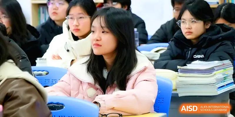 A female student wearing a pink puffer jacket looks on with concentration during a classroom lecture in a modern learning environment at Walton-Hefei School.