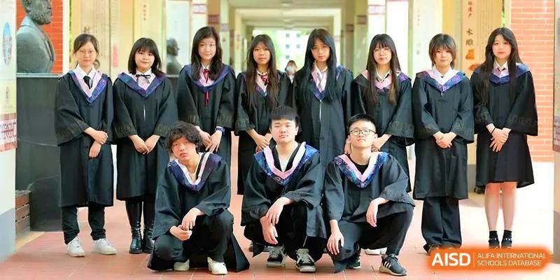 A group of graduating students in black academic gowns and caps poses for a commemorative photo in a sunny campus hallway at Walton-Hefei School.