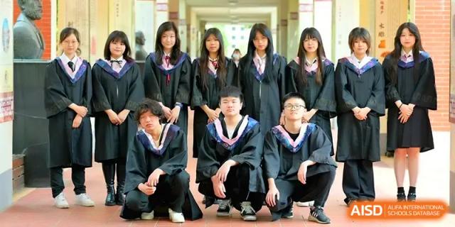 A group of graduating students in black academic gowns and caps poses for a commemorative photo in a sunny campus hallway at Walton-Hefei School.