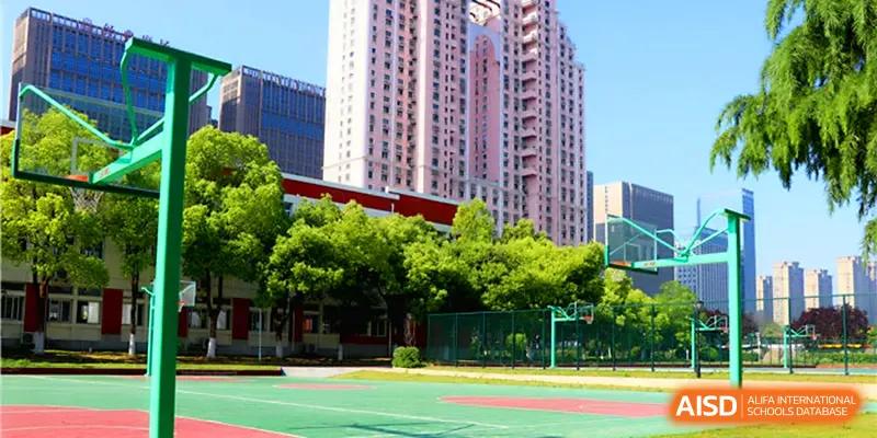 A wide shot of the vibrant green basketball courts and sports facilities located on the modern urban campus of Walton-Hefei School.